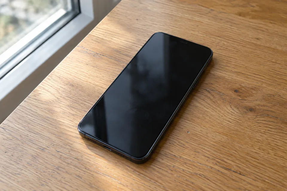 Symbolbild eines unmarkierten Smartphones auf einem Holztisch bei Tageslicht.